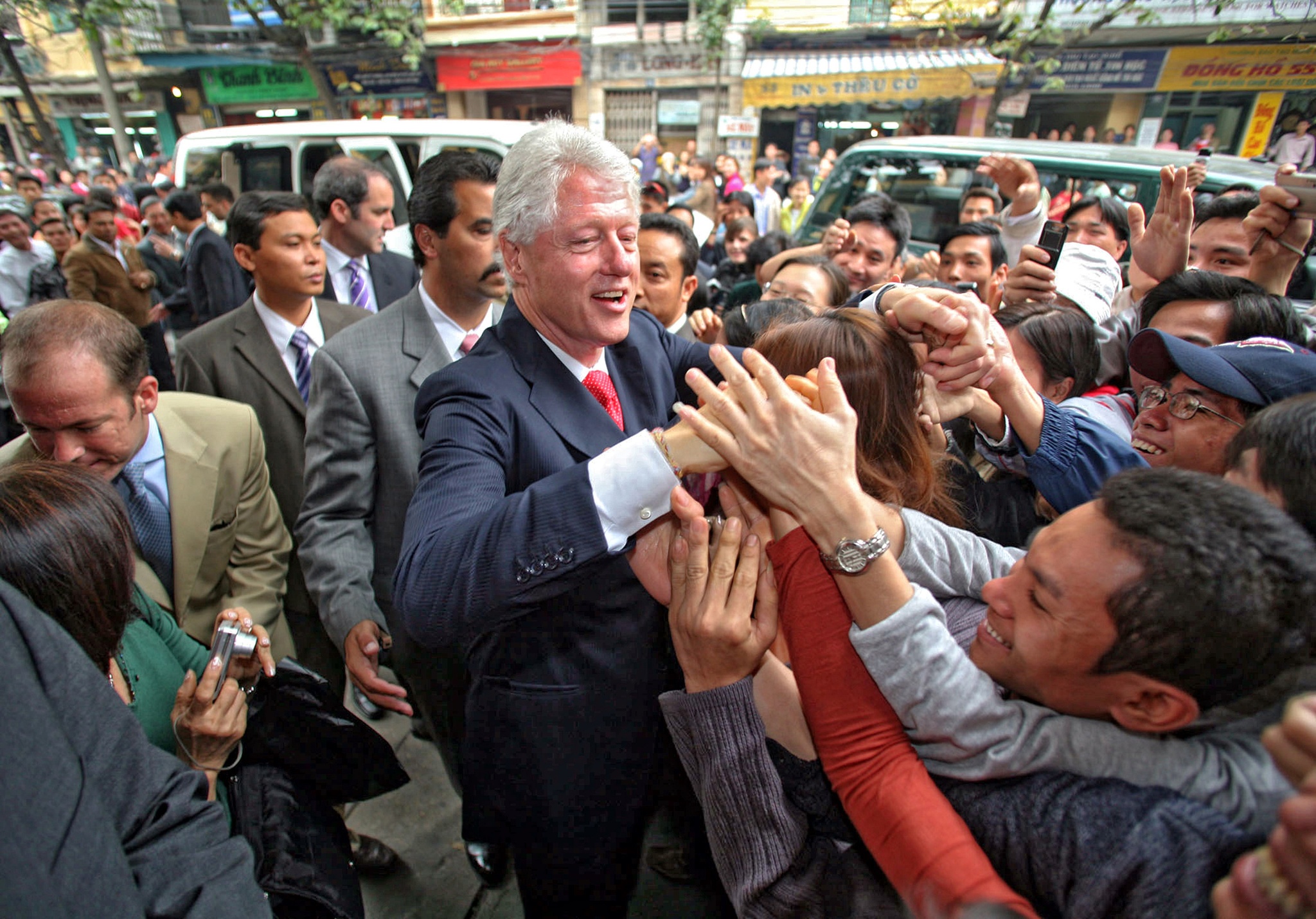 President Bill Clinton shakes hands with Vietnamese people who smile brightly to welcome him.