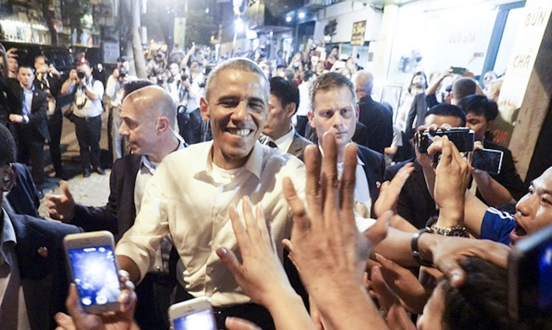 President Obama with a bright smiling face surrounds by excited local Vietnamese people as he goes down the street to greet them.
