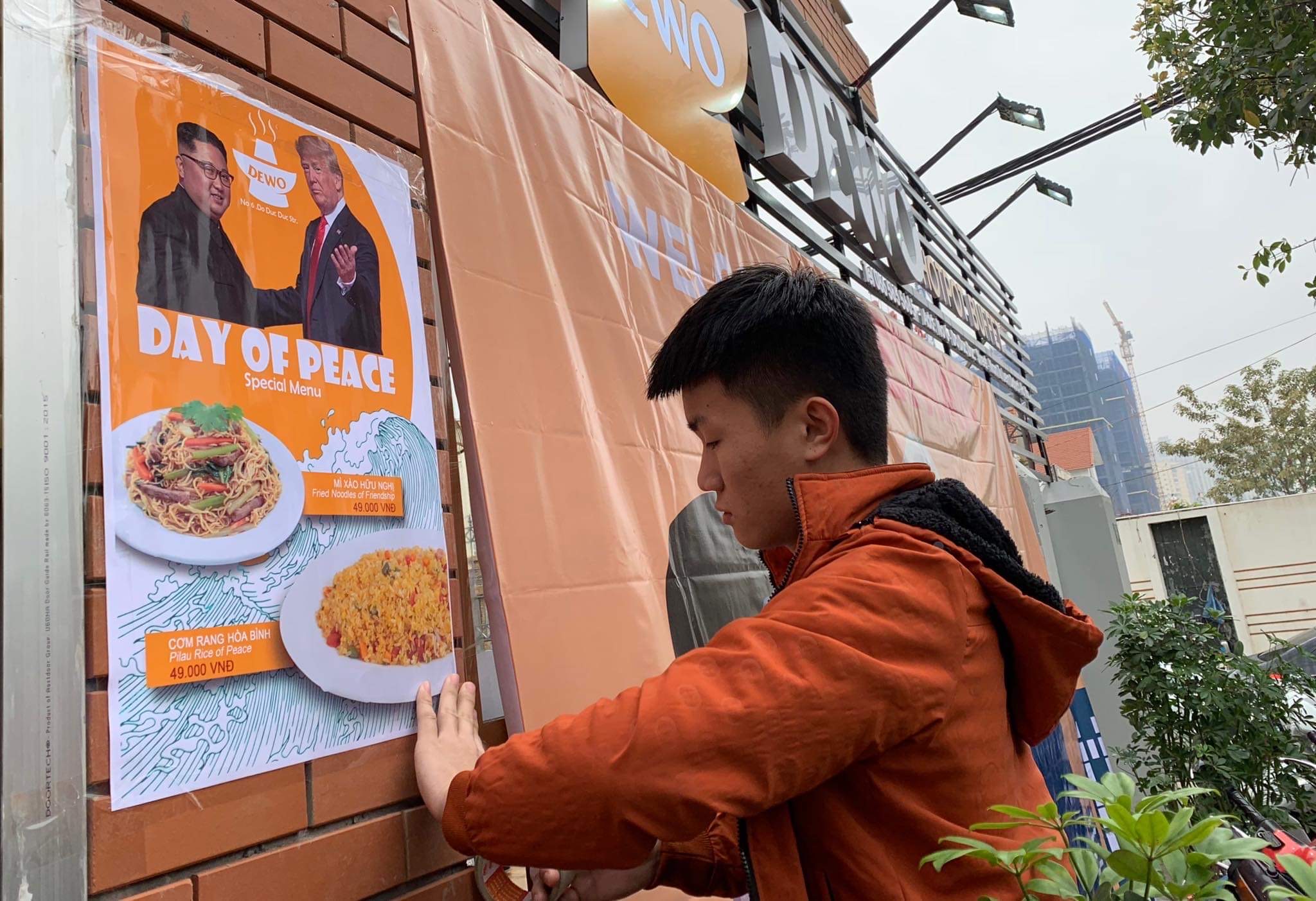 A Vietnamse man is hanging a banner advertise day of Peace's special menu on the wall.