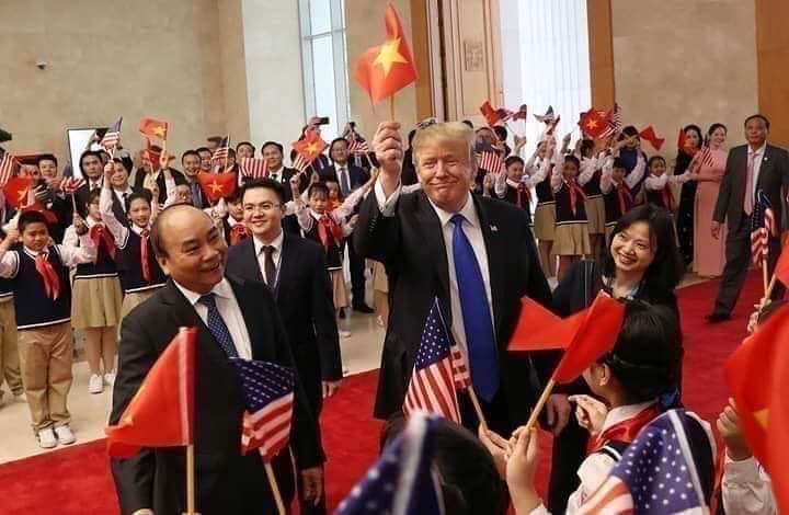 President Trump is waving a Vietnam flag in his hand as he is surrounded by Vietnamese's students who are waving Vietnam's and U.S's flags.