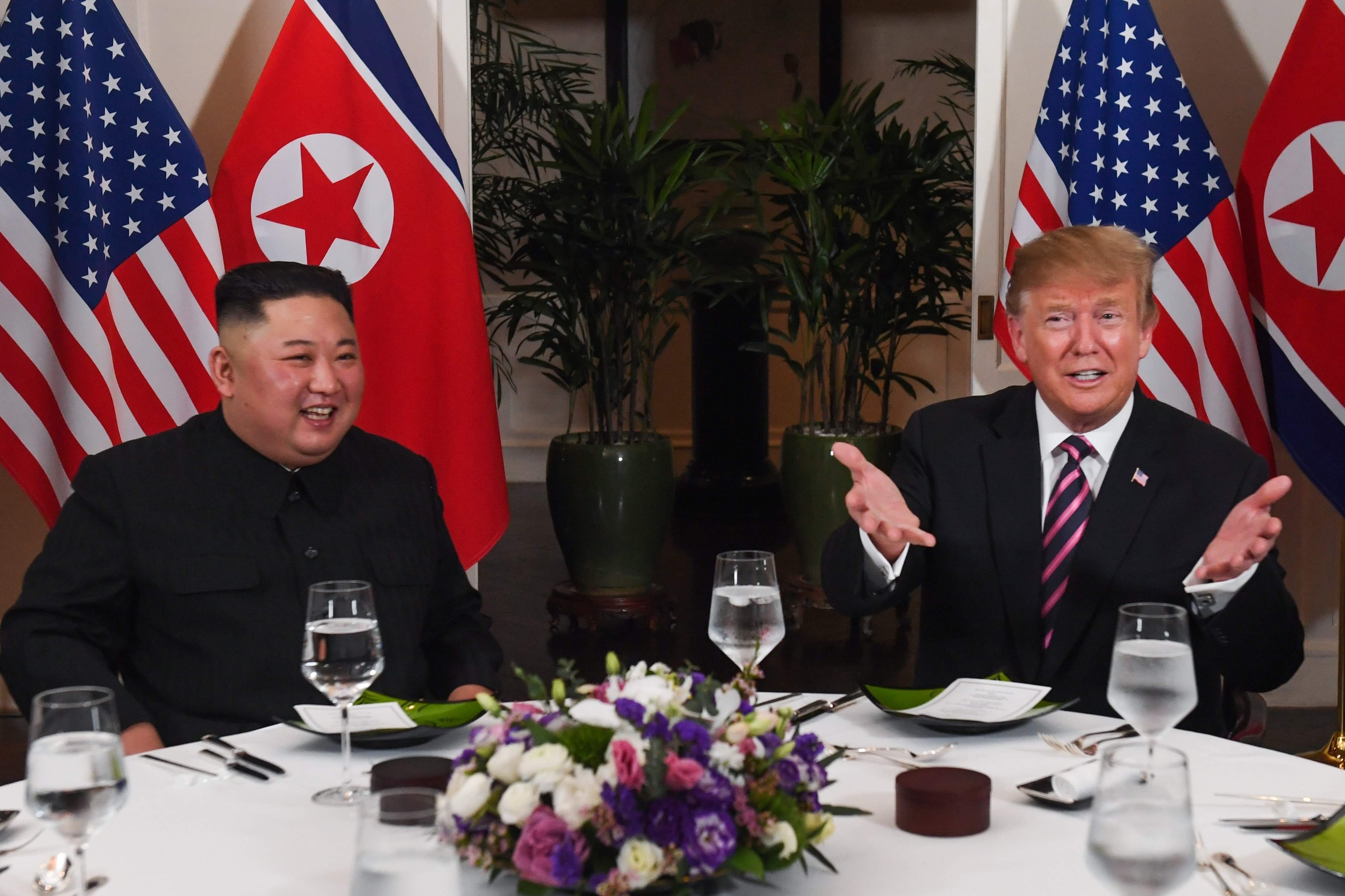 President Trump and DPRK's Chairman Kim Jong Un sit down on a table with smiling faces.