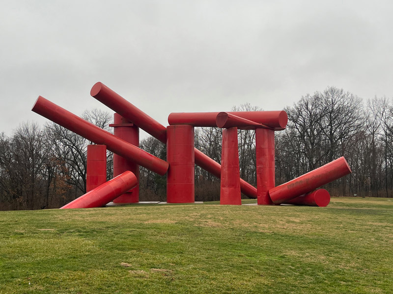 Various red cylinders are stacked around and on top of one another haphazardly on a grassy hill, with the cylinders pointing in different directions.